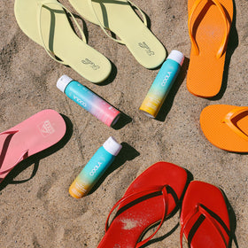 COOLA Organic Sunscreen Spray SPF 50 Guava Mango travel size next to beach accessories