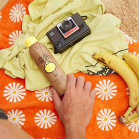 Sun Bum sunscreen spray bottles on a beach towel